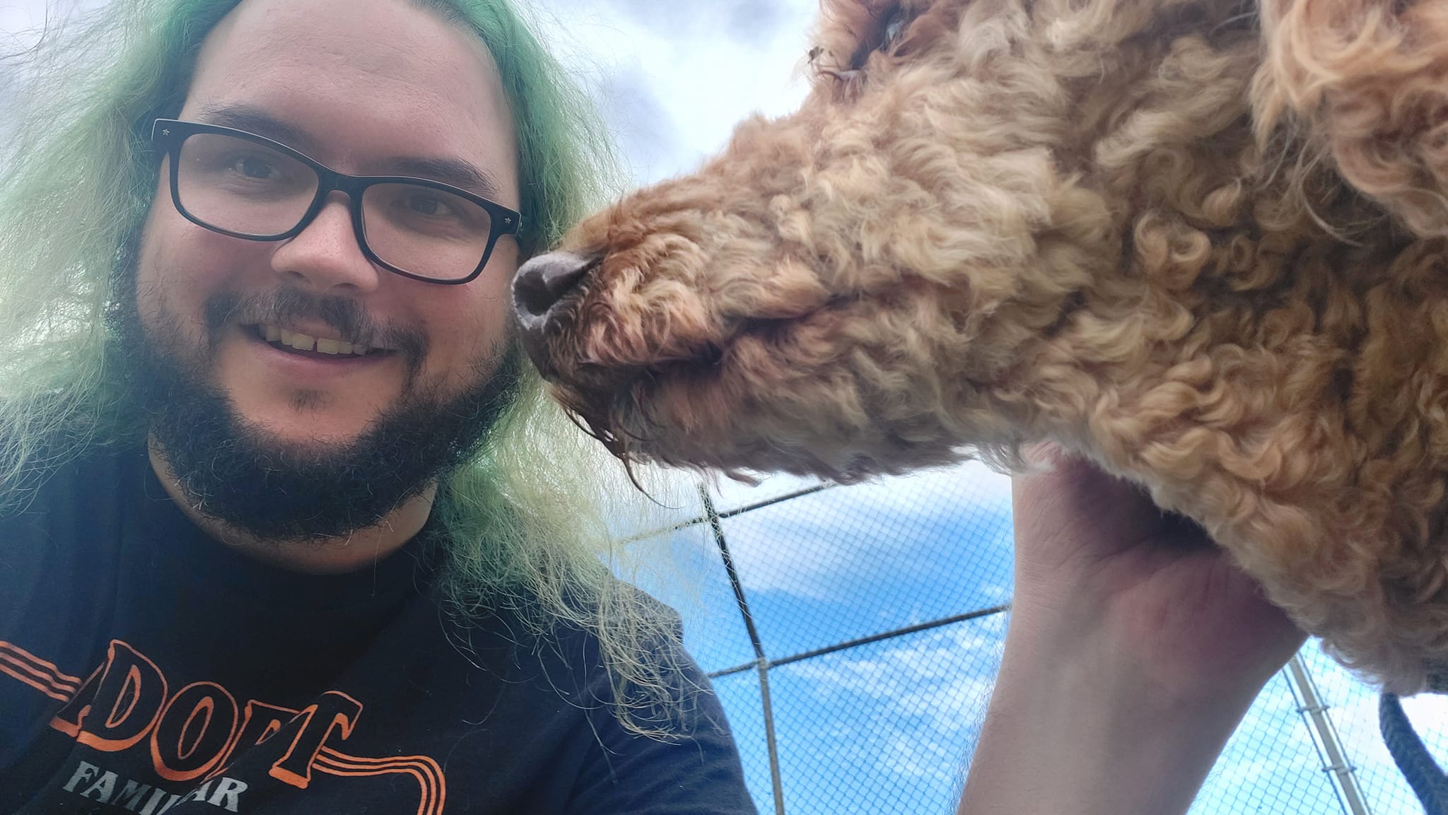 A man with green hair and a beard is outside with a golden standard poodle